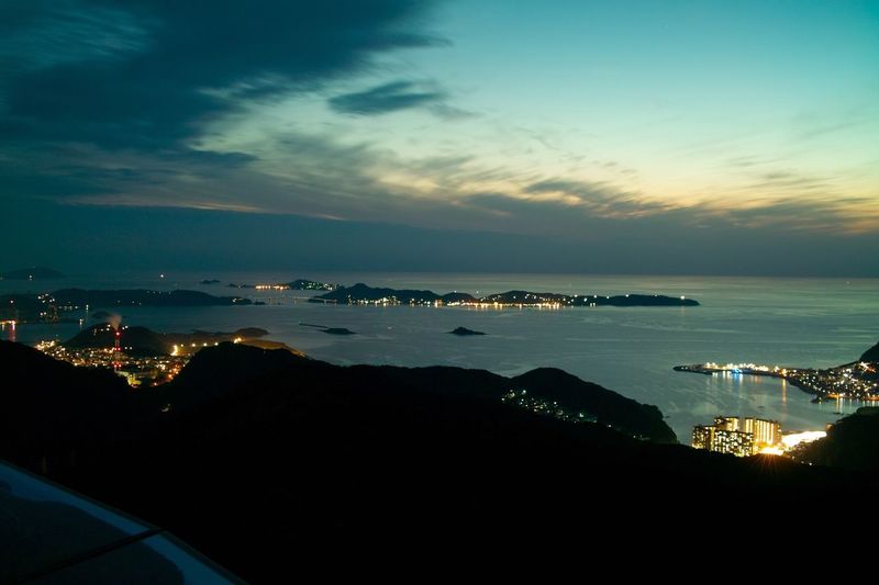 High angle view of illuminated city by sea at sunset