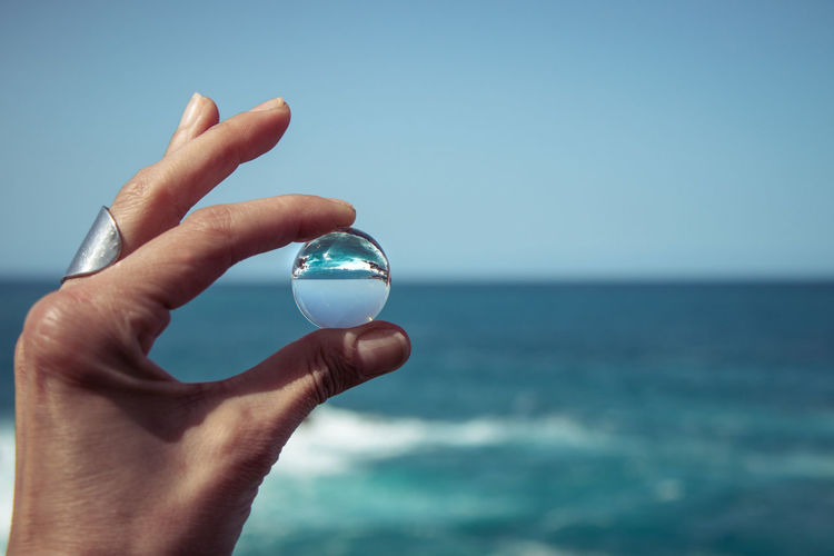 Midsection of person holding crystal ball against sea