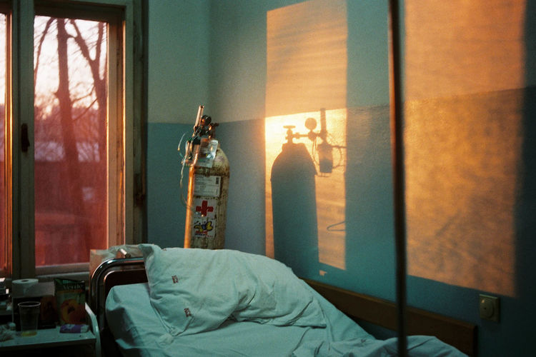Oxygen tank by bed against window in hospital during sunset