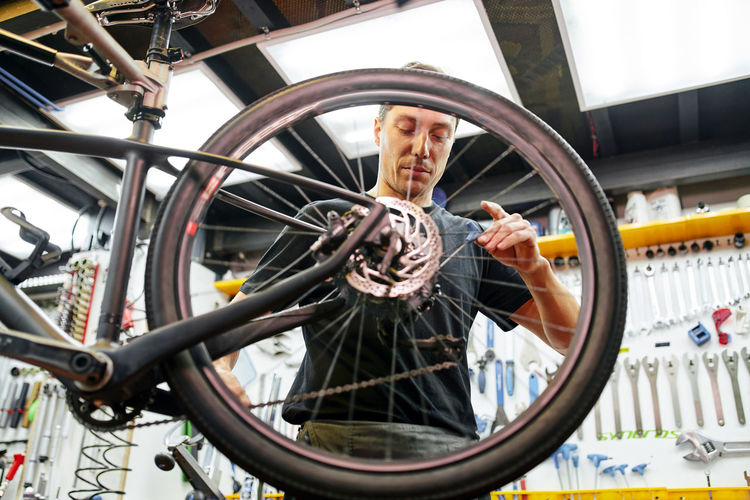Male technician attaching wheel to bike while working in professional modern workshop