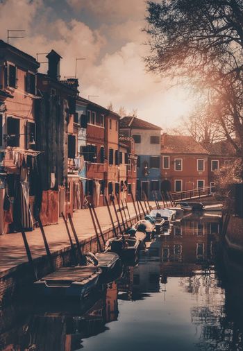 Boats moored in canal by buildings against sky during sunset
