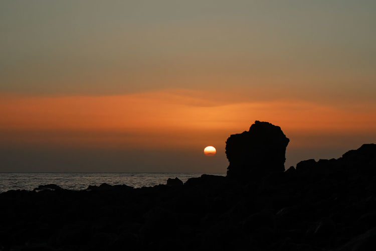 Silhouette rocks by sea against sky during sunset