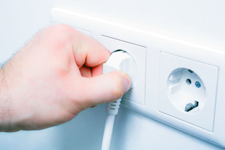 Cropped hand inserting plug in electrical outlet