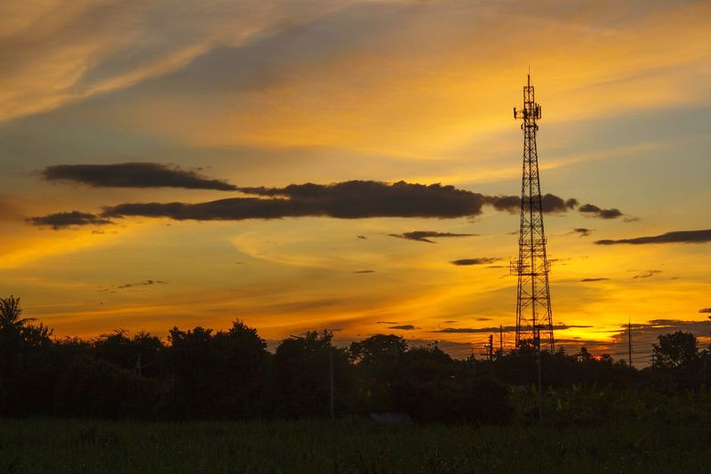 Silhouette of communications tower on field against orange sky