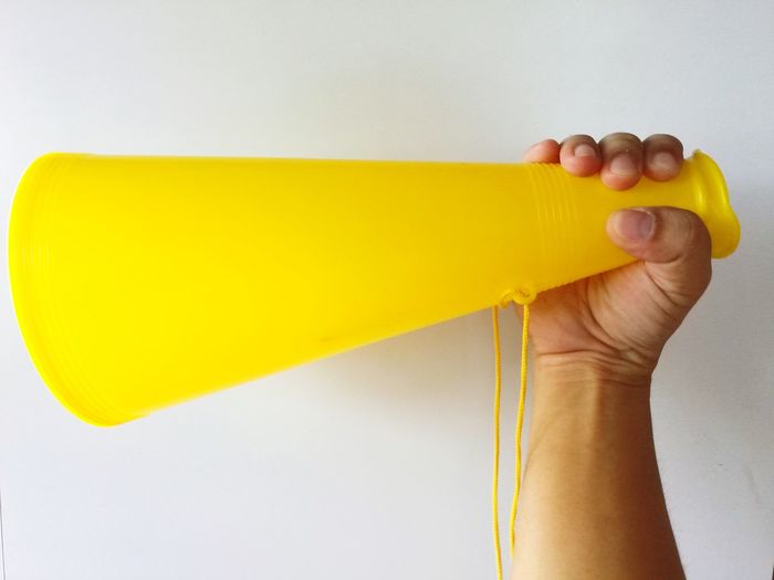 Close-up of hand holding yellow toy against white background
