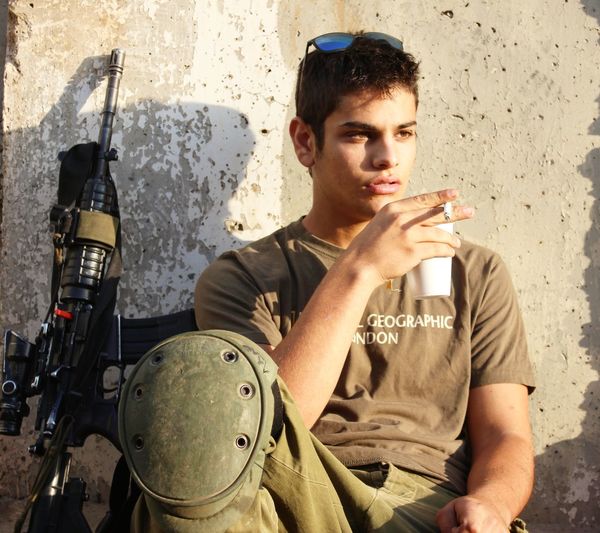 Young man smoking cigarette while sitting by rifle