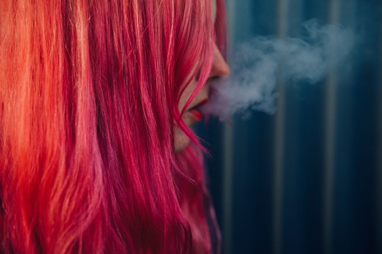 Close-up of woman with dyed hair emitting smoke from mouth