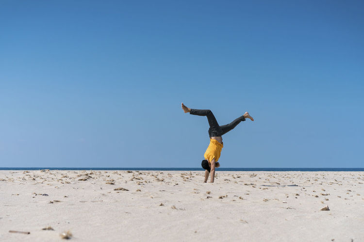 Man doing handstand on beach during sunny day