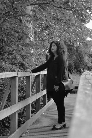 Woman standing on footbridge against trees