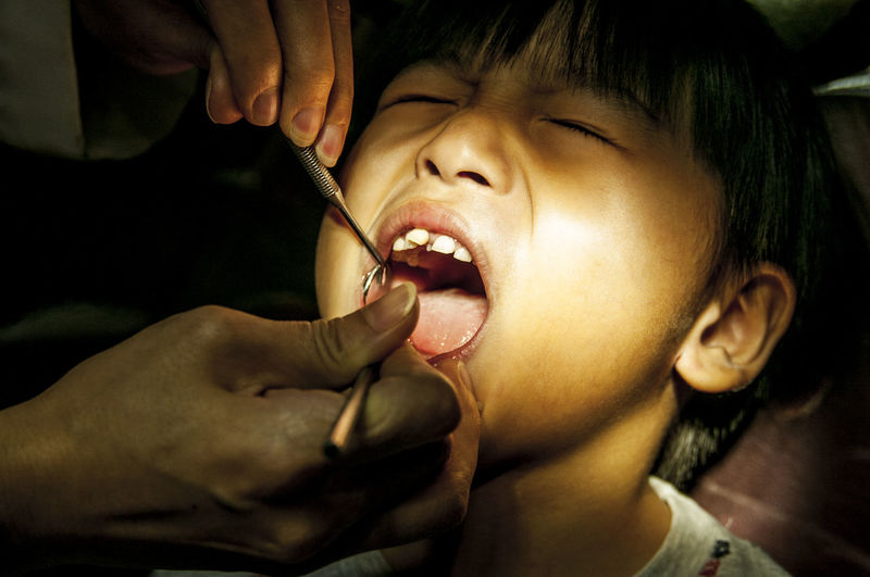 Cropped hand of pediatric dentist examining boy teeth