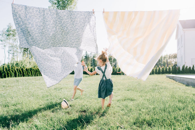 Siblings running through washing in the yard joyfully in summer