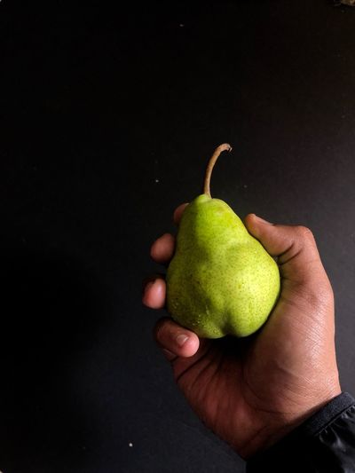 Close-up of hand holding apple against black background
