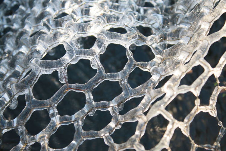 Close up of frozen ice in icicles and hexagon patterns on metal wire cover the frost on garden pond