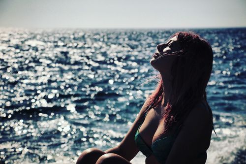 Seductive woman with eyes closed resting at beach during sunny day