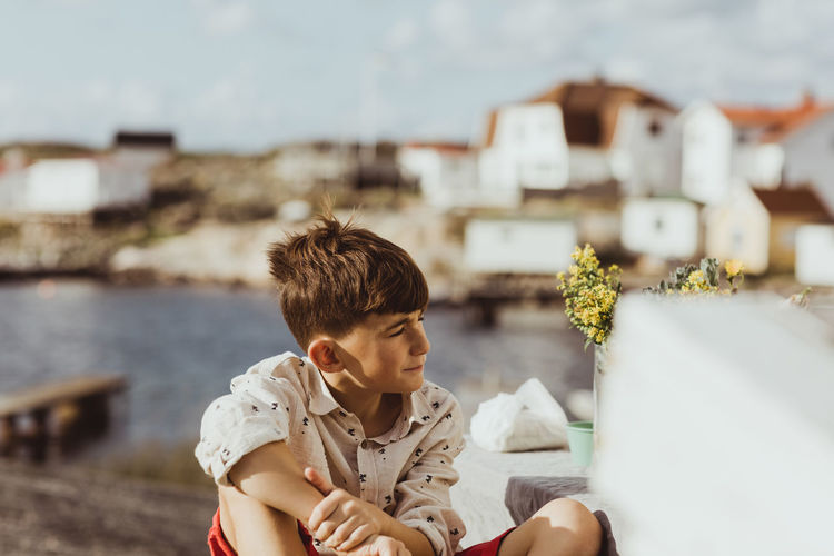 Contemplating boy looking away while sitting outdoors during sunny day