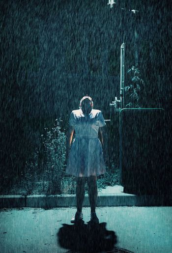 Full length of woman standing on street during rainfall at night