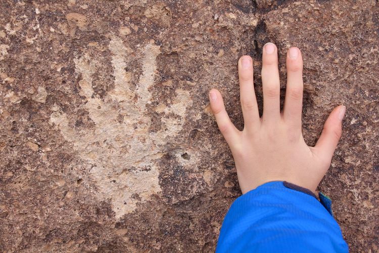 Hand beside handprint on rock