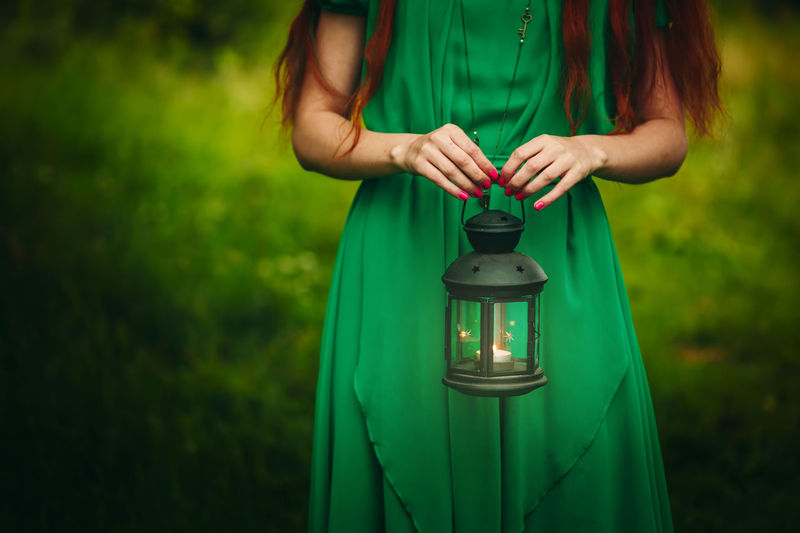 Midsection of woman holding lantern while standing on land