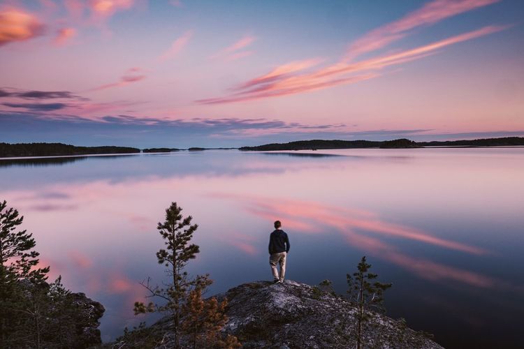 Man standing on rock by lake against sky during sunset