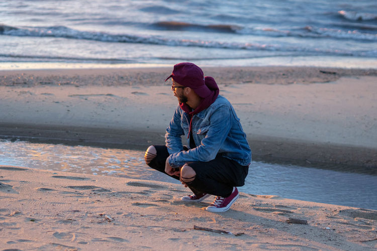 Man crouching at beach during sunset