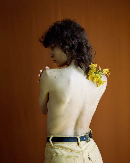 Rear view of shirtless boy standing against wall