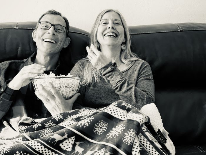 Senior couple laughing and eating popcorn together watching a movie at home.  movie date night.