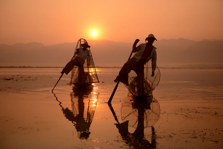 Men fishing in lake at sunset