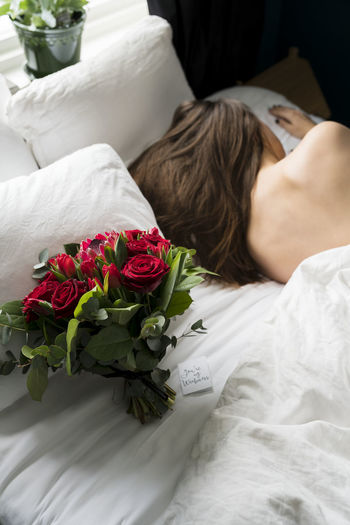 Midsection of woman with rose bouquet on bed