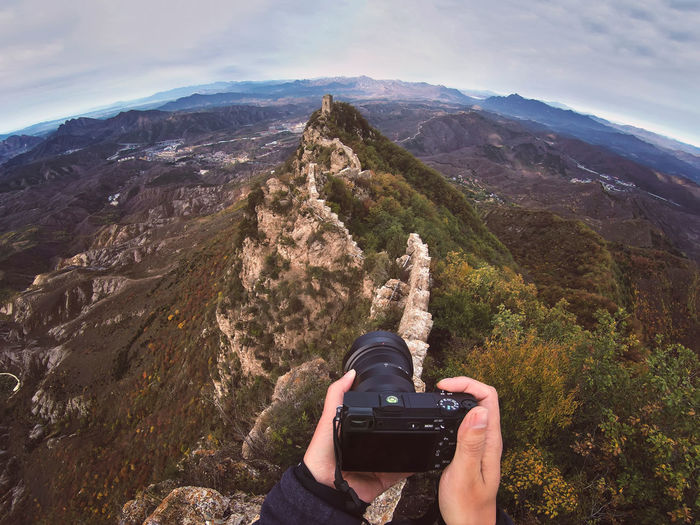 Cropped image of man photographing mountain with camera against sky