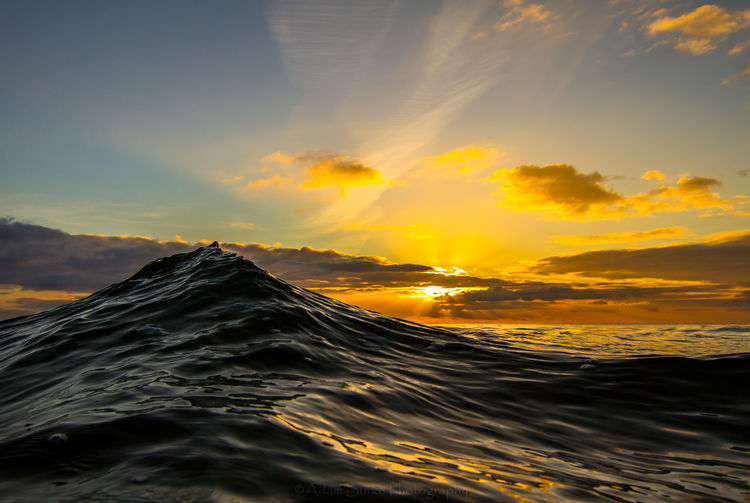 Sea wave against sky at sunset