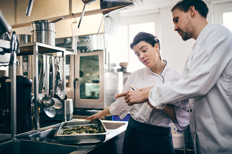 Male and female chefs reading order ticket while preparing food in commercial kitchen