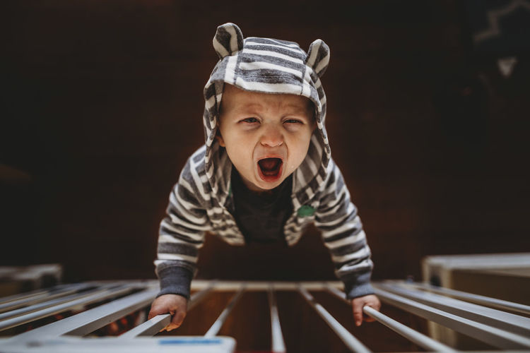 High angle portrait of baby boy crying while standing by railing at home