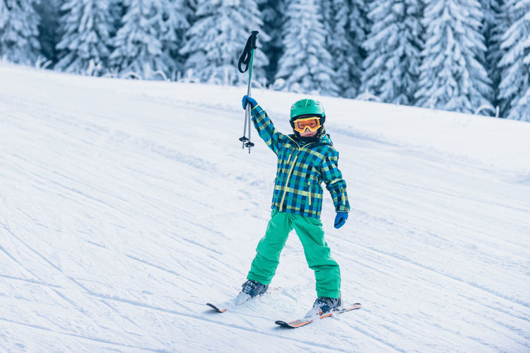 Full length portrait of boy holding ski poles on snow covered land