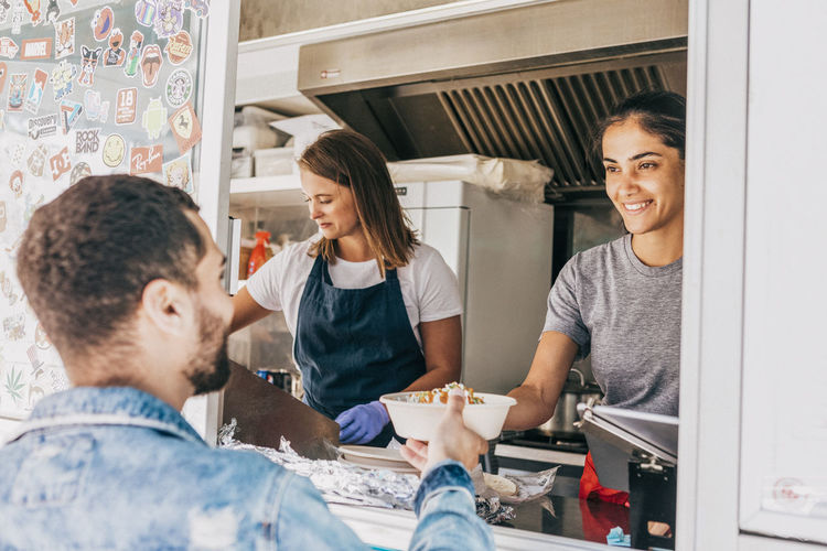 Smiling young female owner giving bowl of tex-mex to male customer from food truck