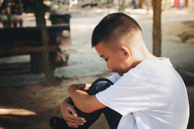 Side view of sad boy sitting outdoors