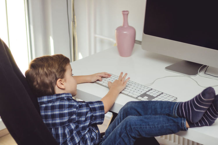 Boy using computer at desk while sitting on swivel chair