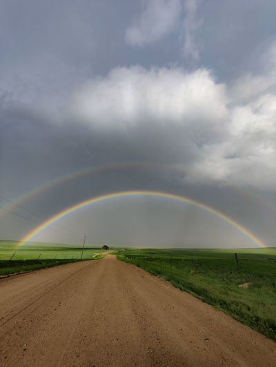 Road amidst field against sky double rainbow 
