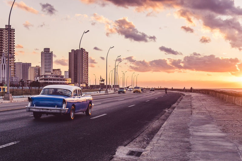 Vehicles on road against sky during sunset
