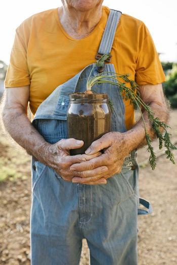 Senior man holding glass jar with soil and growing carrot