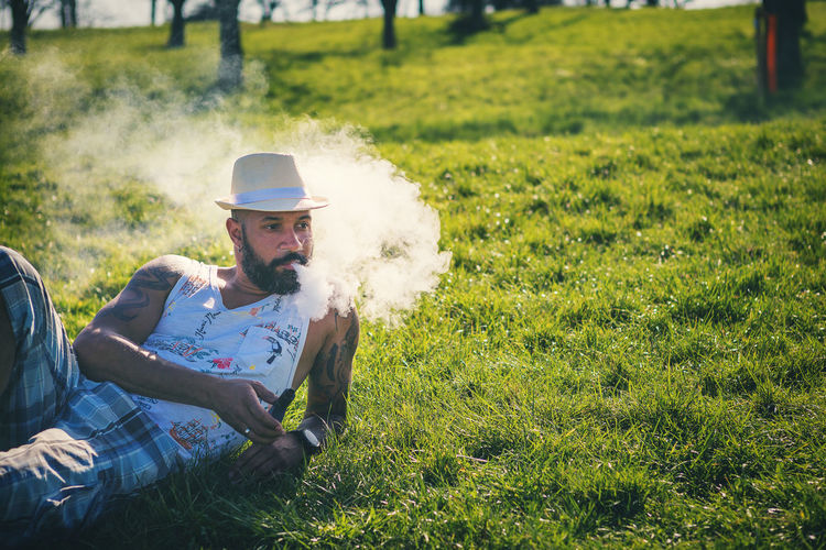 Man smoking electronic cigarette while lying at park