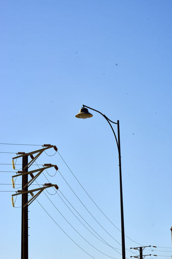 Low angle view of power line and street light against clear blue sky