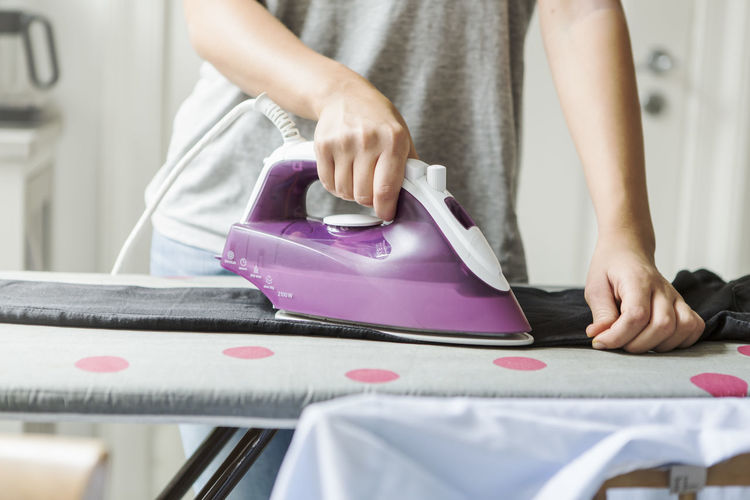 Midsection of teenage girl ironing clothes at home