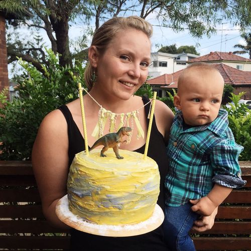 Portrait of smiling mother with cute son holding cake while crouching against plants
