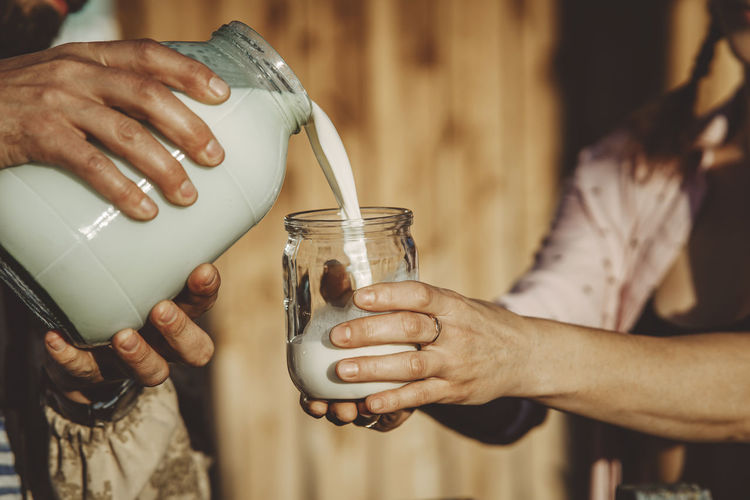 Man pouring fresh milk into glass jar on sunny day