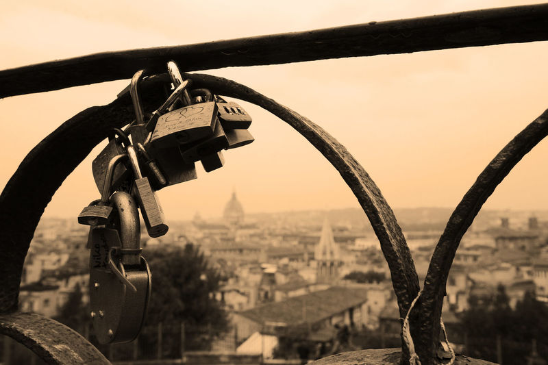 Close-up of padlocks hanging on railing against sky in city