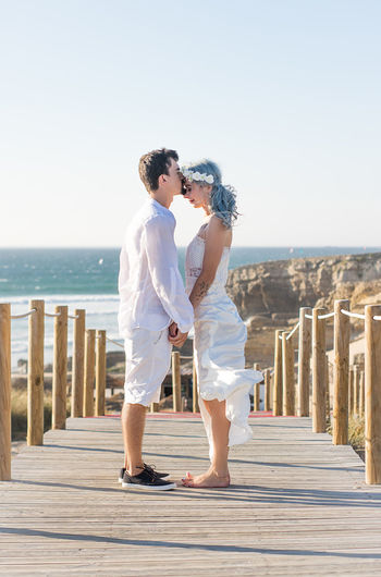 Full length of couple kissing while standing on pier against sky