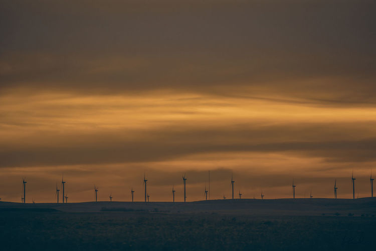 Windmills on field against cloudy sky during sunset