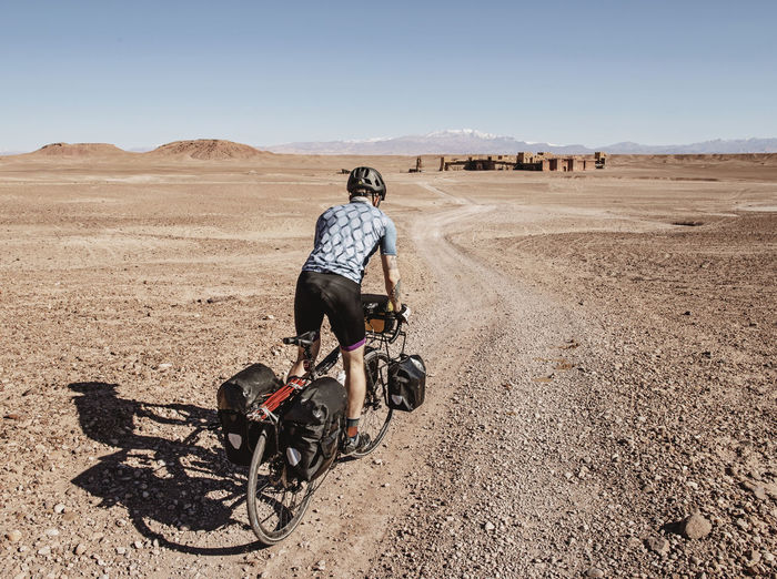 A cyclist rides through a desert toward ruins, ouarzazate, morocco