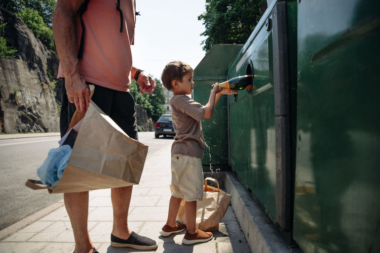 Side view of boy trashing bottle in garbage bin while standing with grandfather