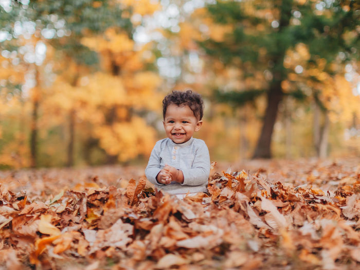 Cute smiling boy sitting on autumn leaf in forest